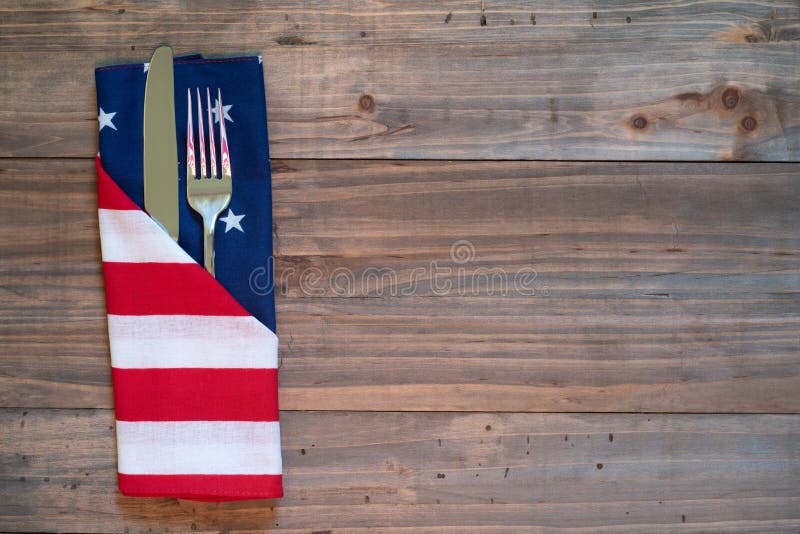 4th of July Rustic Picnic Table Place Setting with silverware and American Flag napkin with background of wood boards for copy space. 4th of July Rustic Picnic Table Place Setting with silverware and American Flag napkin with background of wood boards for copy space