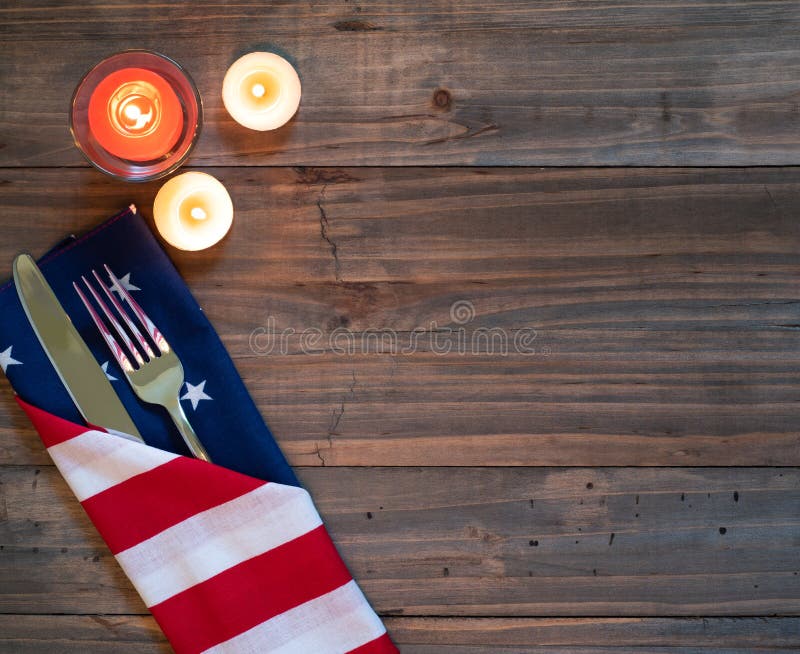 4th of July Rustic Table Placesetting with American flag napkin, silverware and three candles on a wood boards background with room or space for copy, text or words.  It`s a horizontal with a flat layout. 4th of July Rustic Table Placesetting with American flag napkin, silverware and three candles on a wood boards background with room or space for copy, text or words.  It`s a horizontal with a flat layout
