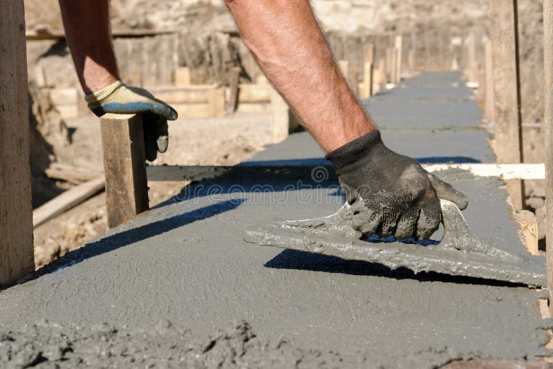 Closeup of mason's hand spreading concrete mix with trowel in foundation shuttering. Closeup of mason's hand spreading concrete mix with trowel in foundation shuttering