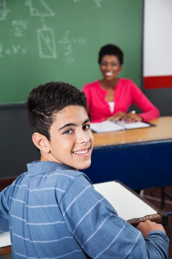 Écolier adolescent heureux s'asseyant au bureau photo stock Écolier adolescent heureux s'asseyant au bureau photo stock