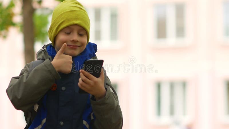 écolier caucasien 79 ans près du bâtiment de l'école communique joyeusement à l'aide d'un smartphone. l'enfant parle via vi