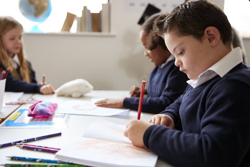 Écolier de la préadolescence avec la trisomie 21 se reposant à un bureau réévaluant dans une classe d'école primaire, fin, vue de photos libres de droits Écolier de la préadolescence avec la trisomie 21 se reposant à un bureau réévaluant dans une classe d'école primaire, fin, vue de photos libres de droits