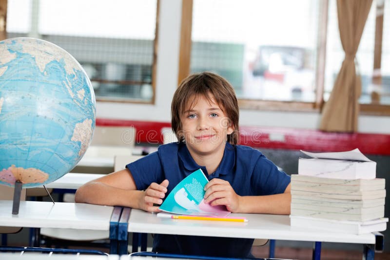 Écolier s'asseyant avec les livres et le globe au bureau image libre de droits Écolier s'asseyant avec les livres et le globe au bureau image libre de droits