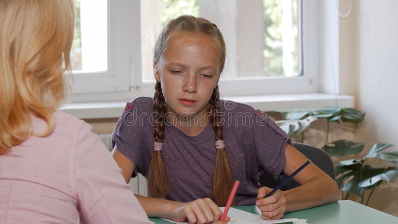 Écolière d'une chevelure rouge mignonne travaillant sur son projet d'art avec l'aide du professeur image libre de droits Écolière d'une chevelure rouge mignonne travaillant sur son projet d'art avec l'aide du professeur image libre de droits