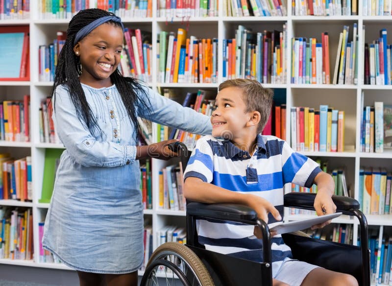 Écolière se tenant avec le garçon handicapé sur le fauteuil roulant photo stock Écolière se tenant avec le garçon handicapé sur le fauteuil roulant photo stock