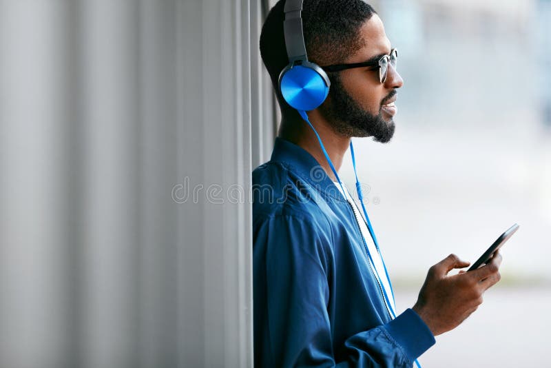 Écoutent la musique Homme avec les écouteurs et le téléphone dans des vêtements de mode photographie stock libre de droits Écoutent la musique Homme avec les écouteurs et le téléphone dans des vêtements de mode photographie stock libre de droits