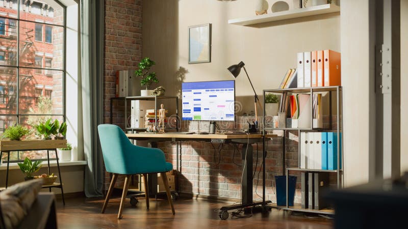 Desktop Computer Monitor Standing on Height Adjustable Desk with Office Software on Display. Cozy Empty Loft Apartment with a Lamp, Notebooks and Smartphone on the Table. Home Office Concept. Desktop Computer Monitor Standing on Height Adjustable Desk with Office Software on Display. Cozy Empty Loft Apartment with a Lamp, Notebooks and Smartphone on the Table. Home Office Concept.