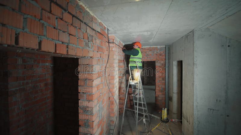 Électricien travaillant sur le câblage dans un bâtiment en construction Un ouvrier du bâtiment dans un gilet de sécurité et un cas banque de vidéos