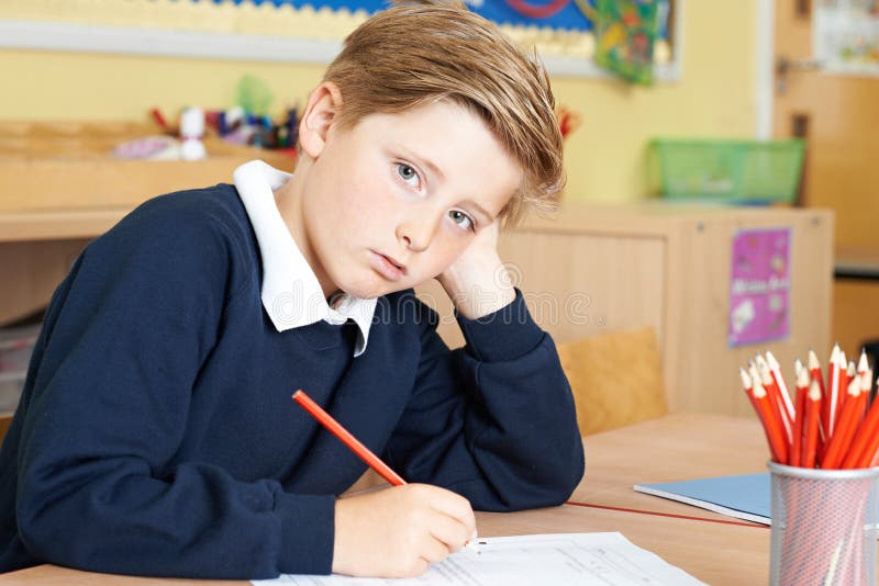 Élève masculin ennuyé d'école primaire au bureau images stock Élève masculin ennuyé d'école primaire au bureau images stock