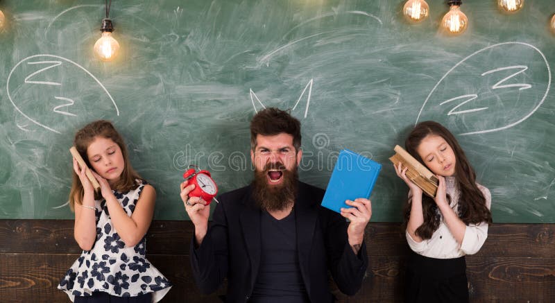 Teacher and girls pupils in classroom, chalkboard on background. Children and teacher with drawn by chalk horns. Horrible lesson concept. Man with beard shouting while schoolgirls pretend sleeping. Teacher and girls pupils in classroom, chalkboard on background. Children and teacher with drawn by chalk horns. Horrible lesson concept. Man with beard shouting while schoolgirls pretend sleeping