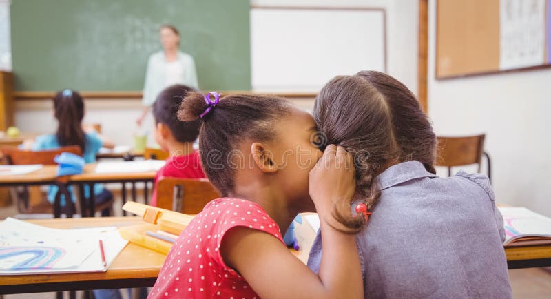 Élèves mignons chuchotant dans la salle de classe photographie stock libre de droits Élèves mignons chuchotant dans la salle de classe photographie stock libre de droits