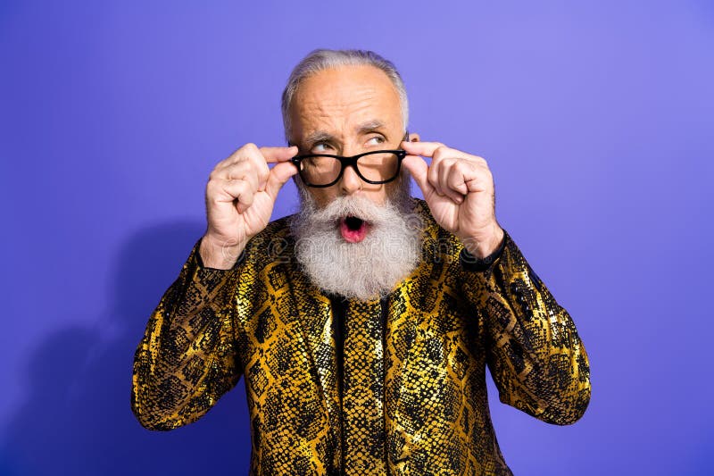 Élégant homme âgé portant une veste à motifs dorés gestes expressivement sur un fond violet vibrant photographie stock