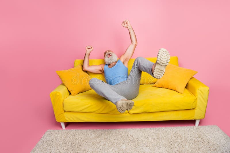 Énergétique riant homme senior sur un élégant canapé jaune avec fond rose photos stock
