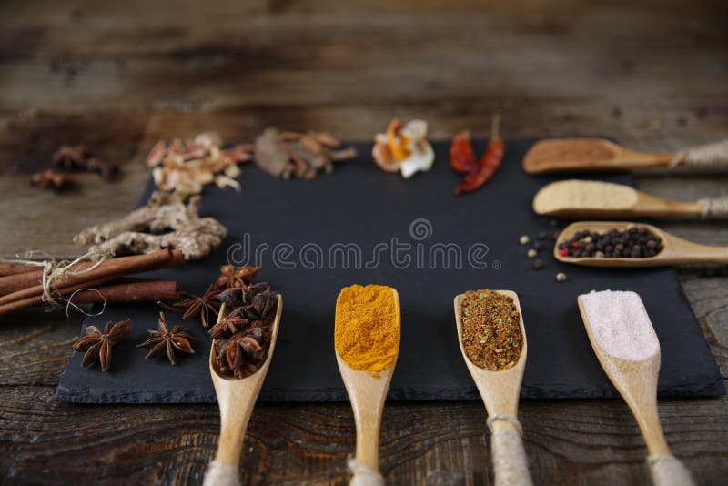 Épices traditionnelles dans des cuillères en bois sur une planche à découper noire sur un fond rustique en bois avec l'espace de photographie stock libre de droits Épices traditionnelles dans des cuillères en bois sur une planche à découper noire sur un fond rustique en bois avec l'espace de photographie stock libre de droits