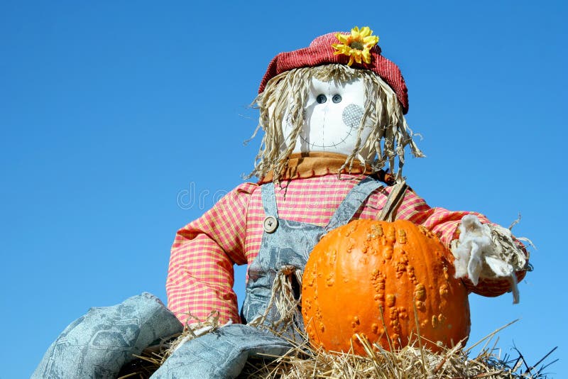 Vivid blue sky is the background for a homemade scarecrow sitting beside a pumpkin on hay. Vivid blue sky is the background for a homemade scarecrow sitting beside a pumpkin on hay.