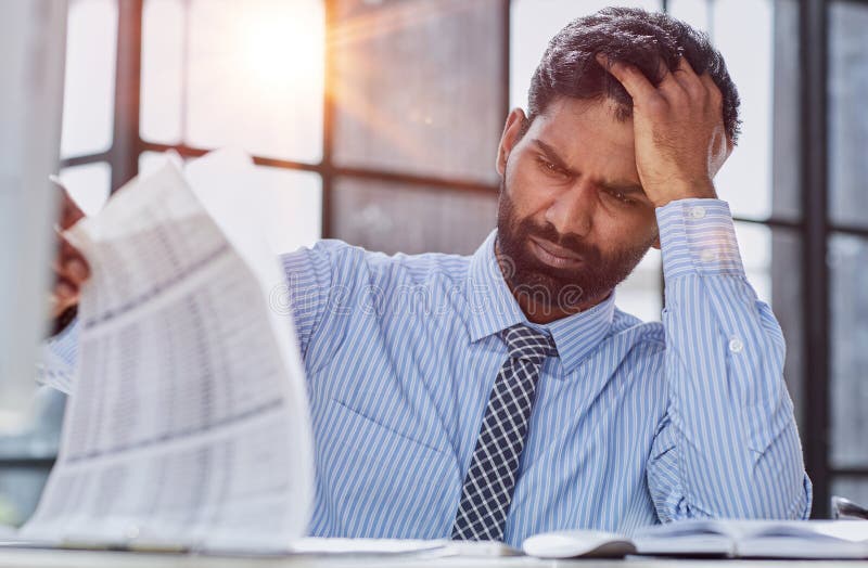 Frustrated overwhelmed executive working in the office and overloaded with paperwork, he is leaning on his arm and feeling depressed. Frustrated overwhelmed executive working in the office and overloaded with paperwork, he is leaning on his arm and feeling depressed