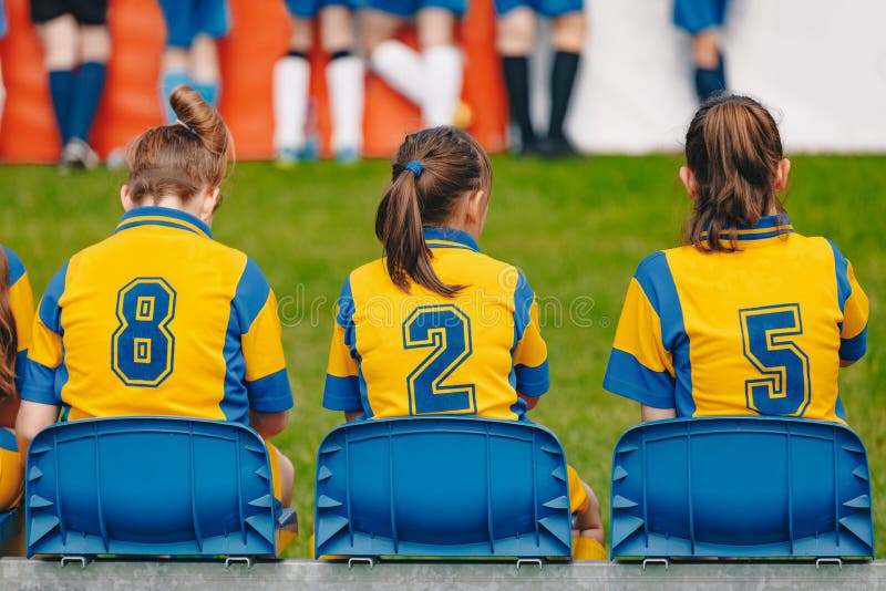 Équipe de sports d'école primaire de filles d'enfants s'asseyant sur le banc sur le champ d'herbe Équipe junior de filles du foot