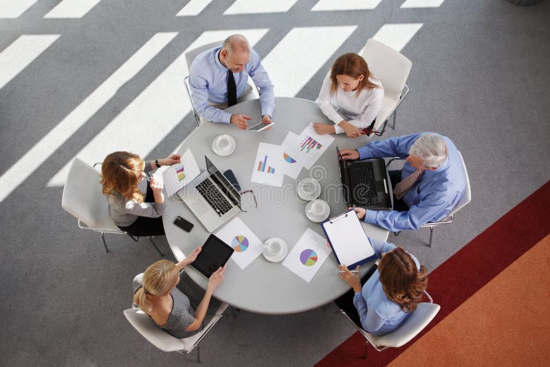 High angle view of business people discussing in a meeting while sitting at conference table. Using digital tablet and computer while analyzing financial data. Aerial shot taken from directly above the table. High angle view of business people discussing in a meeting while sitting at conference table. Using digital tablet and computer while analyzing financial data. Aerial shot taken from directly above the table.