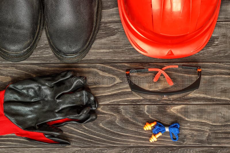 Personal protective equipment: black gloves protect the glasses of the helmet on a wooden background. Personal protective equipment: black gloves protect the glasses of the helmet on a wooden background.