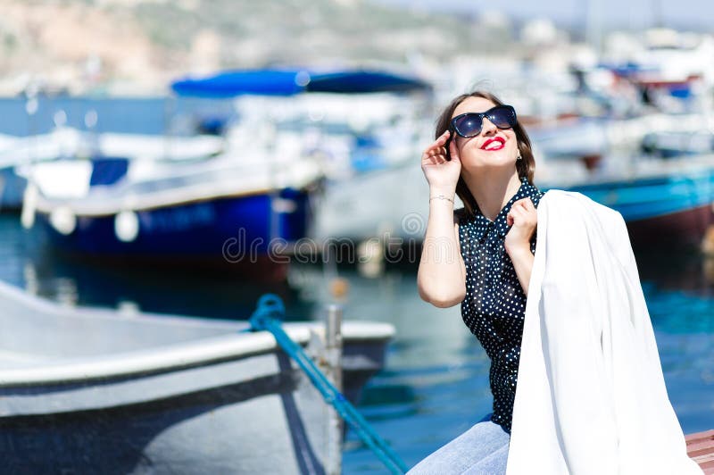 Équipement de whilte de mode de belle femme riante à la mode dans des lunettes de soleil posant sur le fond marin de bateaux photo stock Équipement de whilte de mode de belle femme riante à la mode dans des lunettes de soleil posant sur le fond marin de bateaux photo stock