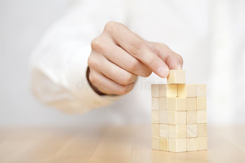 Man`s hand adding the last missing wooden block into place. Business success concept. Man`s hand adding the last missing wooden block into place. Business success concept.