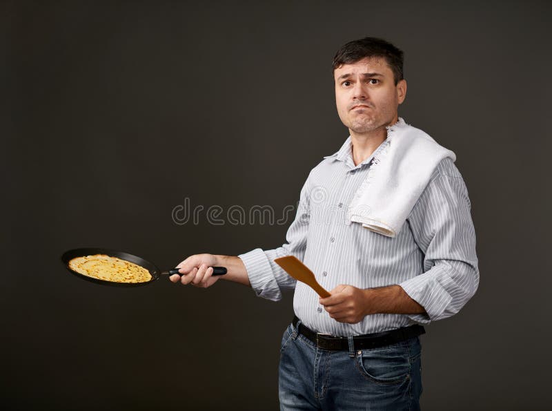 Équipez la pose avec une crêpe dans une casserole, une chemise blanche et un pantalon, fond gris, émotions étonnées photos libres de droits Équipez la pose avec une crêpe dans une casserole, une chemise blanche et un pantalon, fond gris, émotions étonnées photos libres de droits