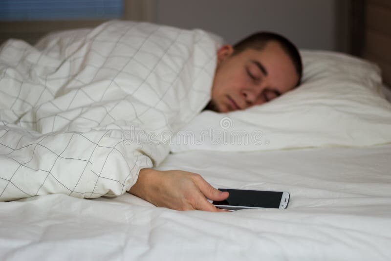 Équipez le sommeil dans le lit et tenir un téléphone portable photos stock Équipez le sommeil dans le lit et tenir un téléphone portable photos stock