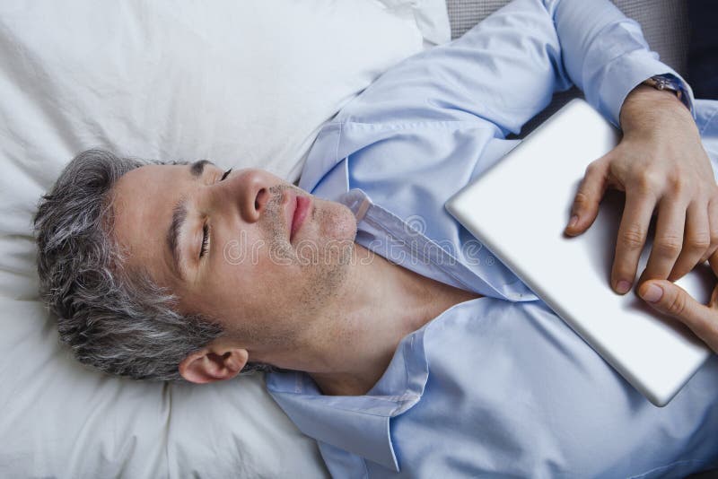 Équipez le sommeil sur le lit avec tenir un comprimé numérique photographie stock