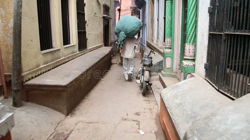 Équipez rapporter un grand sac sur le sien dans la rue étroite à Varanasi, vue arrière clips vidéos