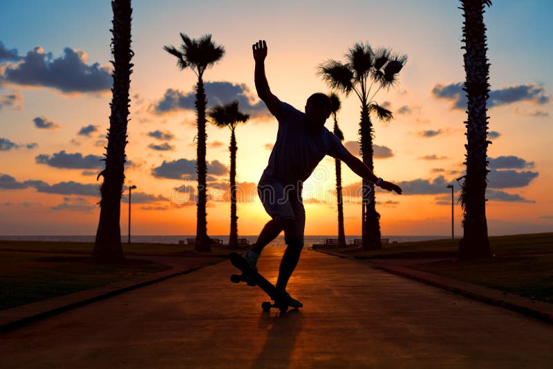 Équitation d'homme sur la planche à roulettes dans le coucher du soleil image stock Équitation d'homme sur la planche à roulettes dans le coucher du soleil image stock