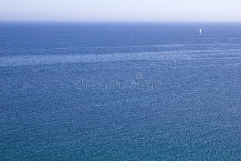 Étendue de l'eau bleue de la mer avec un voilier blanc à l'horizon photographie stock libre de droits Étendue de l'eau bleue de la mer avec un voilier blanc à l'horizon photographie stock libre de droits