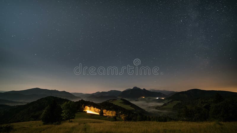 Étoiles se déplaçant en ciel nocturne au-dessus des montagnes et de paysage rural brumeux au clair de lune Nuit au tir de chariot