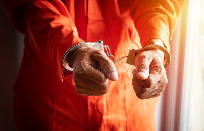 Étroitement des mains du prisonnier avec des menottes dans la salopette orange à la prison photographie stock Étroitement des mains du prisonnier avec des menottes dans la salopette orange à la prison photographie stock