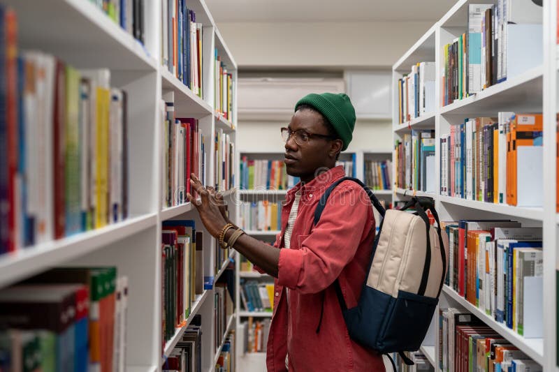 étudiant africain réfléchi homme en lunettes choisir livre dans la bibliothèque de collège ou librairie photo libre de droits