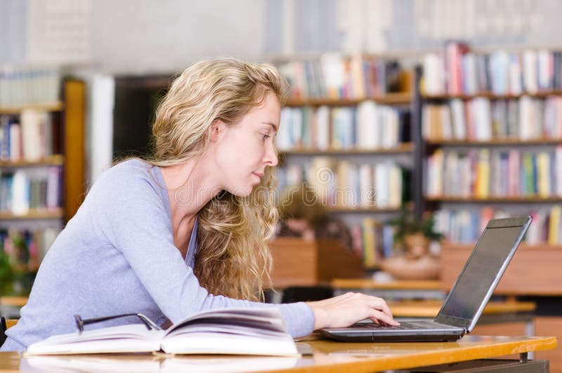 Étudiant avec l'ordinateur portable fonctionnant dans la bibliothèque images stock