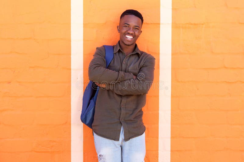 Étudiant masculin africain heureux se tenant contre le mur orange avec le sac image stock Étudiant masculin africain heureux se tenant contre le mur orange avec le sac image stock