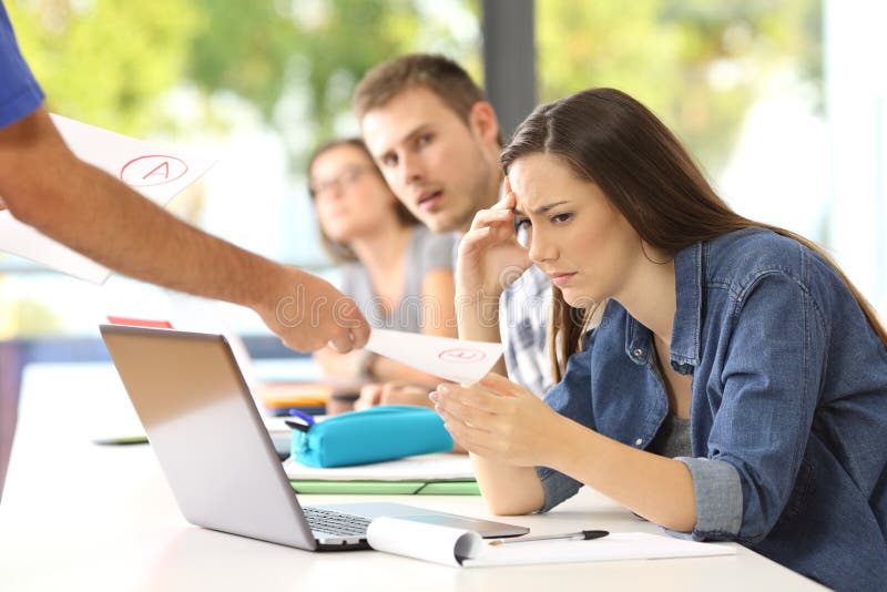 Sad student receiving a failed exam in a classroom with classmates watching in the background. Sad student receiving a failed exam in a classroom with classmates watching in the background