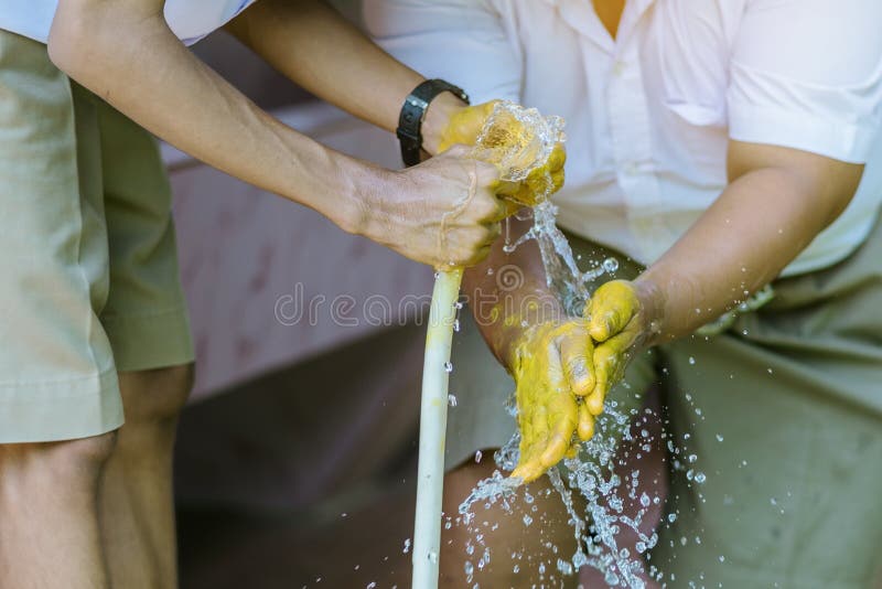 Étudiant tenant un tuyau de jardin vaporisant de l'eau du tube de caoutchouc blanc pour se laver les mains tachées image stock Étudiant tenant un tuyau de jardin vaporisant de l'eau du tube de caoutchouc blanc pour se laver les mains tachées image stock