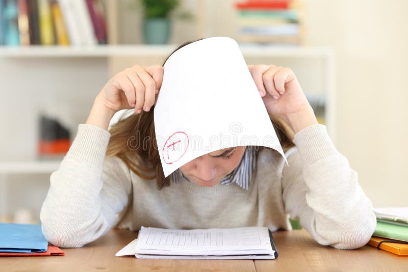 Front view of a sad student covering head with a failed exam at home. Front view of a sad student covering head with a failed exam at home
