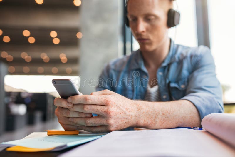 Étudiant à l'aide du téléphone portable dans la bibliothèque photographie stock Étudiant à l'aide du téléphone portable dans la bibliothèque photographie stock