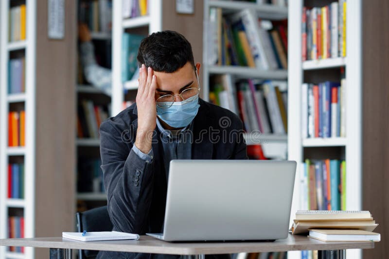 étudiant étudiant étudiant à la bibliothèque utilisant un ordinateur portable pendant une pandémie. étudiant portant lunettes et masque de protection travail sur ordinateur portable dans la bibliothèque navigation internet faire des devoirs personne floue sur fond prise de livre de bibliothèque. éducation en cas de pandémie
