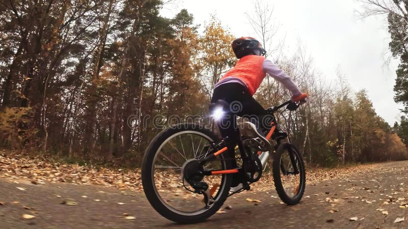 Één Kaukasische de fietsweg van kinderenritten in de herfstpark Het meisje die zwarte oranje cyclus in bosjong geitje berijden ga