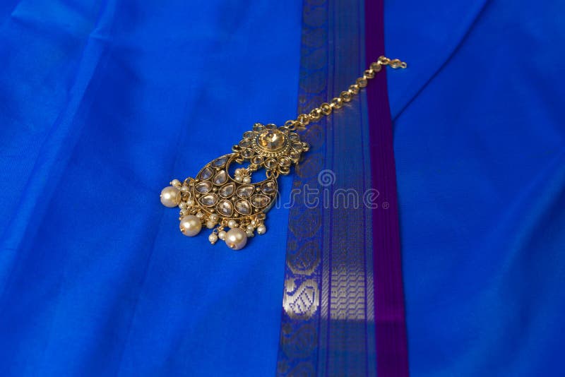 Indian traditional gold Indian wedding women`s jewelry tika on blue saree background. Close-up. Still-life. Indian traditional gold Indian wedding women`s jewelry tika on blue saree background. Close-up. Still-life.