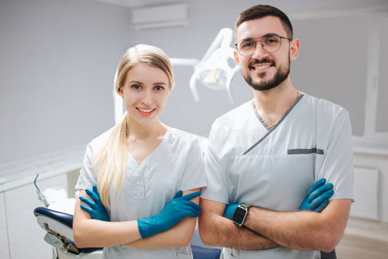Δύο νέοι επαγγελματίες οδοντιάτρων στο δωμάτιο οδοντιατρικής Θέτουν στο camer και το χαμόγελο Οι άνθρωποι κρατούν τα χέρια διασχι στοκ εικόνες Δύο νέοι επαγγελματίες οδοντιάτρων στο δωμάτιο οδοντιατρικής Θέτουν στο camer και το χαμόγελο Οι άνθρωποι κρατούν τα χέρια διασχι στοκ εικόνες