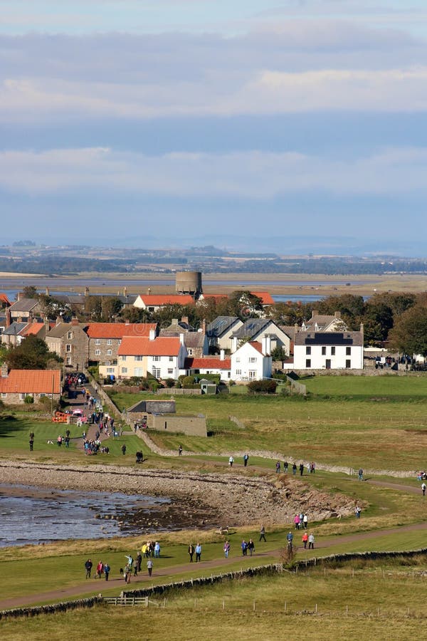 View west across Holy Island from Lindisfarne Castle to Lindisfarne village, Holy Island, Northumberland with the mainland in the background and visitors walking to and from the castle in the foreground. View west across Holy Island from Lindisfarne Castle to Lindisfarne village, Holy Island, Northumberland with the mainland in the background and visitors walking to and from the castle in the foreground.