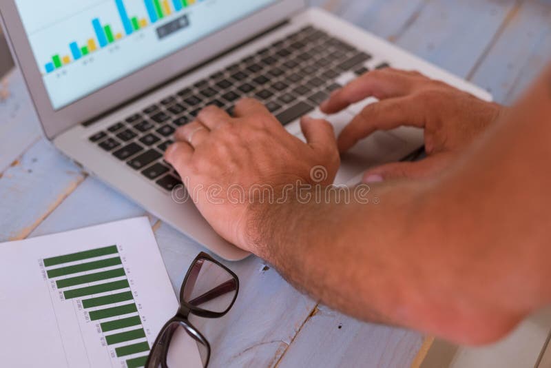 închiderea mâinilor unui om care utilizează un om de afaceri notebook care se uită la graficele de pe ecran și de pe masă stock photos