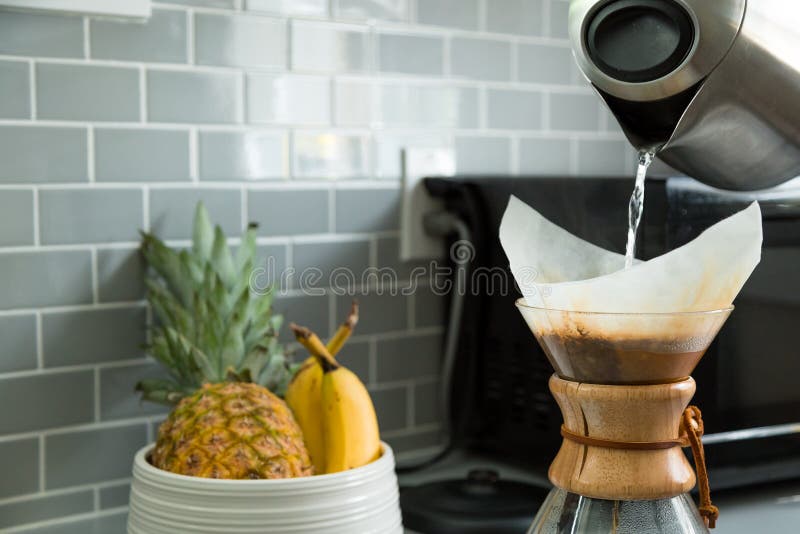 învelișul unui ceainic electric care toarnă apă caldă într-un balon de cafea cu picurător cu un bol de fructe în fond. stock photo