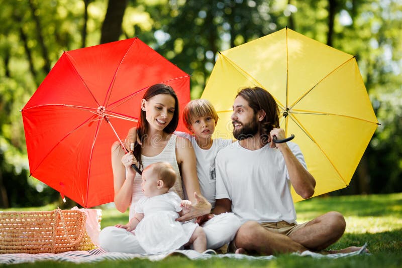 Αστεία παιδιά με το mom και τη συνεδρίαση μπαμπάδων στο κάλυμμα κάτω από τις μεγάλες κόκκινες και κίτρινες ομπρέλες που καλύπτουν στοκ φωτογραφίες με δικαίωμα ελεύθερης χρήσης Αστεία παιδιά με το mom και τη συνεδρίαση μπαμπάδων στο κάλυμμα κάτω από τις μεγάλες κόκκινες και κίτρινες ομπρέλες που καλύπτουν στοκ φωτογραφίες με δικαίωμα ελεύθερης χρήσης