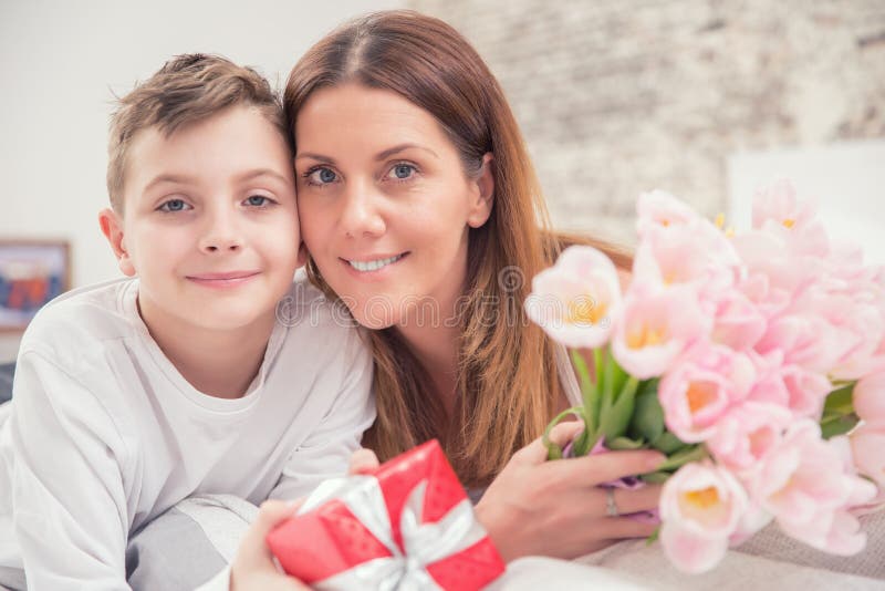 Ευτυχής έννοια ημέρας μητέρων ` s Mom με το γιο στο κρεβάτι με το δώρο και τις τουλίπες στοκ εικόνα Ευτυχής έννοια ημέρας μητέρων ` s Mom με το γιο στο κρεβάτι με το δώρο και τις τουλίπες στοκ εικόνα