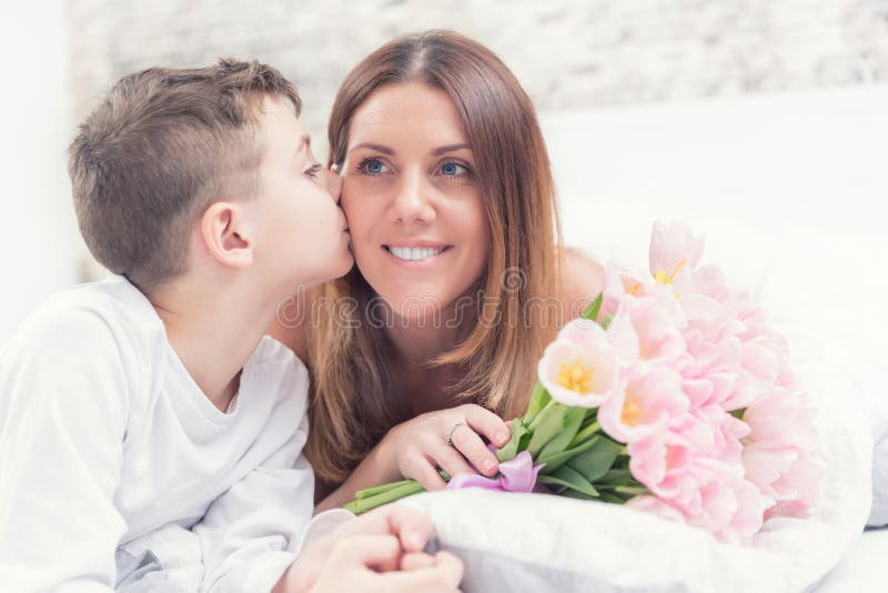 Ευτυχής έννοια ημέρας μητέρων ` s Mom με το γιο στο κρεβάτι με το δώρο και τις τουλίπες Ο γιος φιλά το mom του στοκ εικόνα με δικαίωμα ελεύθερης χρήσης Ευτυχής έννοια ημέρας μητέρων ` s Mom με το γιο στο κρεβάτι με το δώρο και τις τουλίπες Ο γιος φιλά το mom του στοκ εικόνα με δικαίωμα ελεύθερης χρήσης